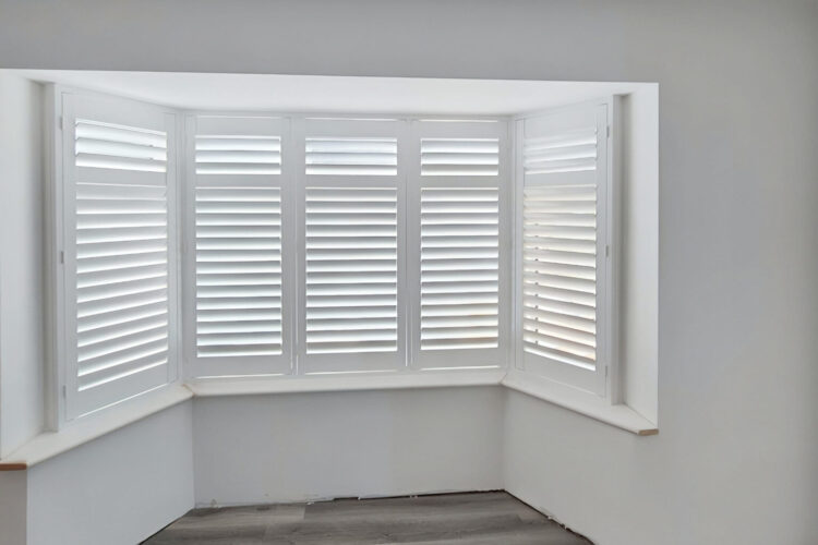 Beautifully fitted UK made white PVC plantation shutters installed in an angled bay window, custom made for a perfect fit.