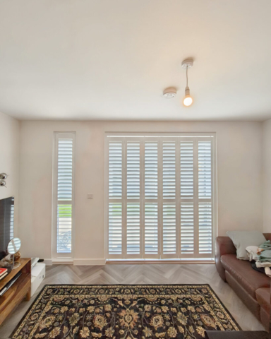 UK Made PVC Plantation Shutters for Long Living Room Windows Beautifully fitted UK made white PVC plantation shutters installed in a living room with long windows by Scarlet Blinds in Manchester, custom made for a perfect fit.