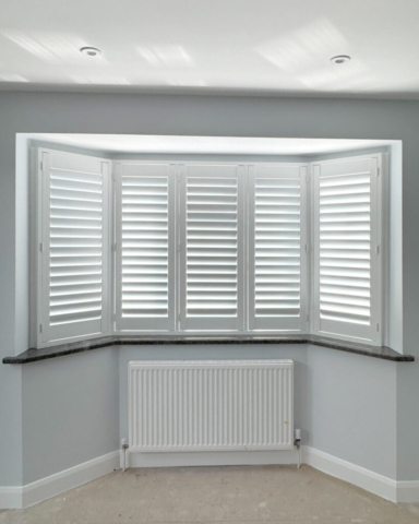 White PVC Plantation Shutters Fitted to Angled Bay Window White PVC plantation shutters fitted to an angled bay window, custom made to follow the window shape and provide privacy and light control.