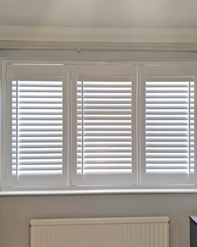 White PVC Plantation Shutters with Centre Control Rod by Scarlet Blinds White PVC plantation shutters with a centre control rod installed in a room by Scarlet Blinds